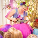 A woman in fairy garment playing a guitar with a group of kids.