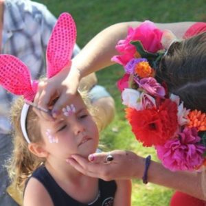 A little girl is getting her face painted with bunny ears.