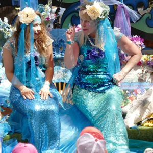 mermaid stage square Two women dressed as mermaids sitting on a blanket.