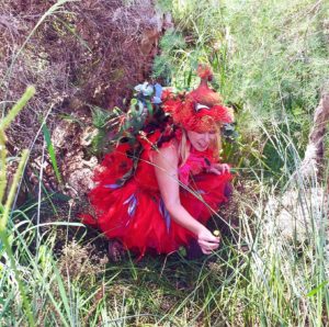A woman in a red dress kneeling in the grass.