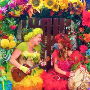 Two women dressed up in flower costumes playing a ukulele.