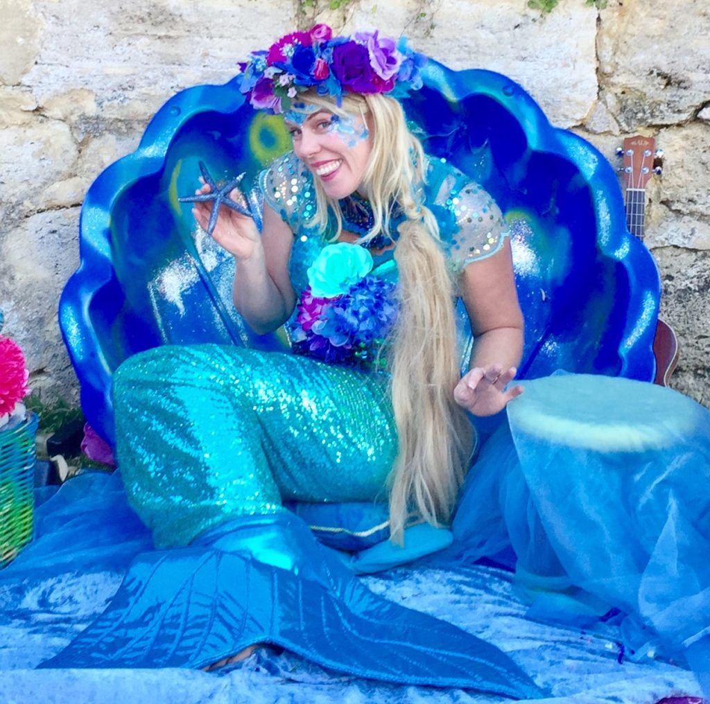 Mermaid Sandie square A woman dressed as a mermaid sitting on a blue shell.