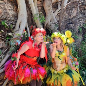 Two women dressed as fairy posing in front of a tree.